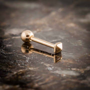 14k rose gold pyramid cartilage stud resting on dark stone surface, angled lifestyle product shot