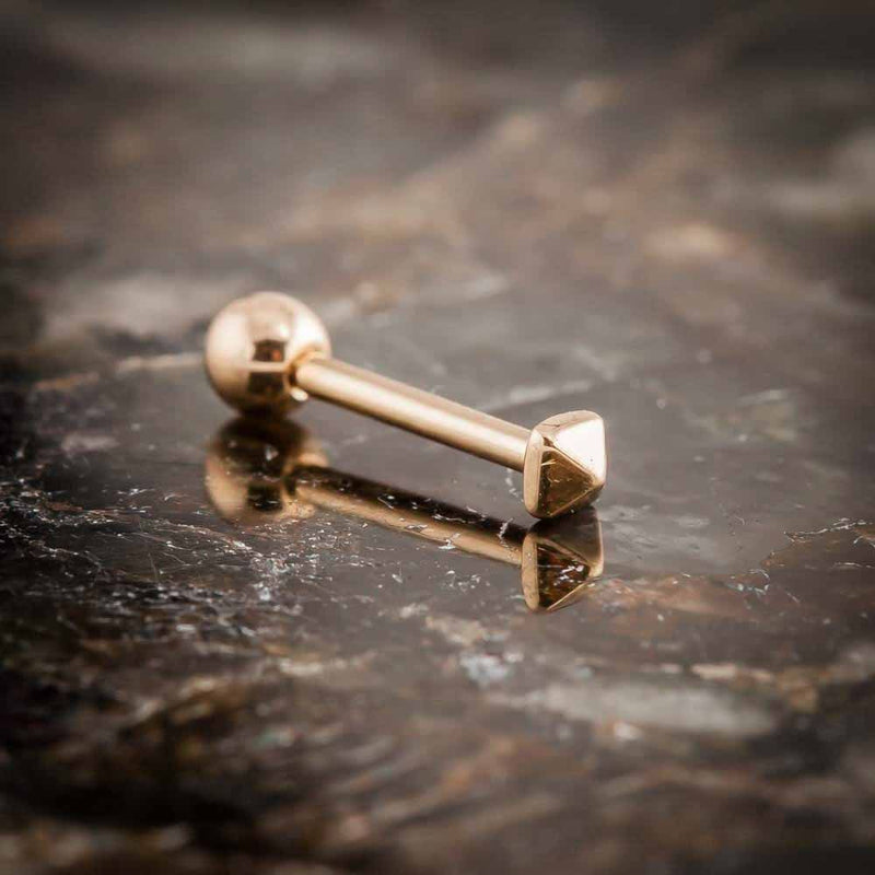 14k rose gold pyramid cartilage stud resting on dark stone surface, angled lifestyle product shot