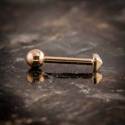 14k rose gold pyramid cartilage stud lying flat on dark stone, full barbell length and ball back visible