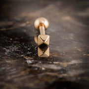 Close-up of 14k rose gold pyramid cartilage stud on dark stone, showing faceted geometric charm detail