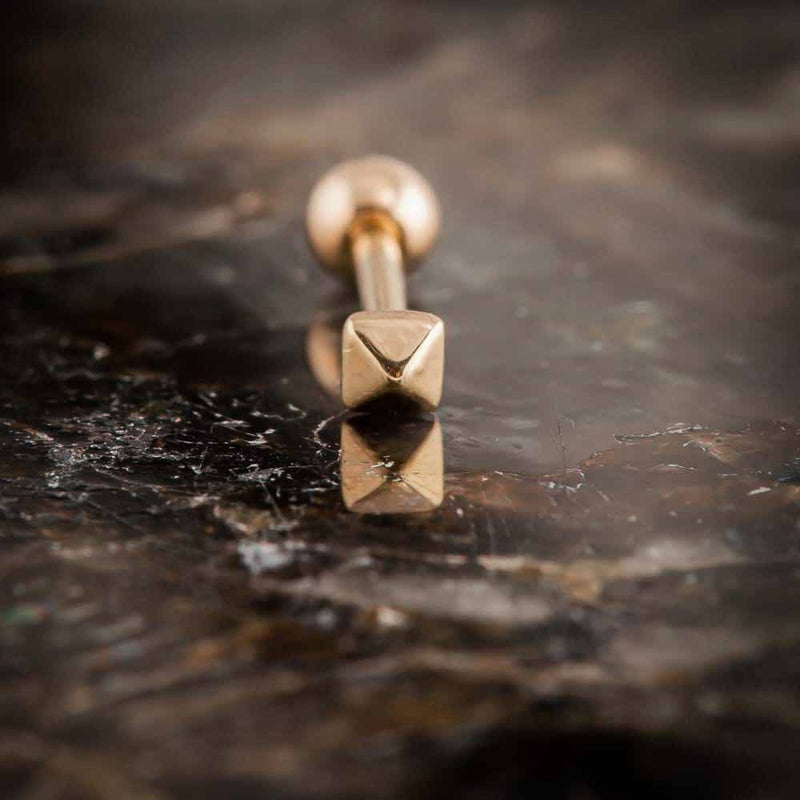 Close-up of 14k rose gold pyramid cartilage stud on dark stone, showing faceted geometric charm detail
