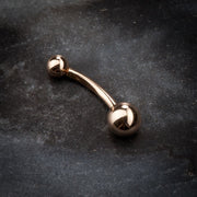 14k rose gold classic double ball belly ring on dark stone surface, angled product view
