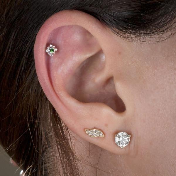 Beaded bezel birthstone cartilage stud with green gem shown in model's upper ear piercing