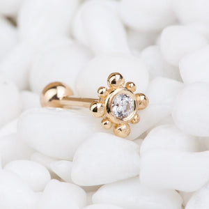 14k rose gold beaded bezel CZ cartilage earring resting on white pebbles, lifestyle shot