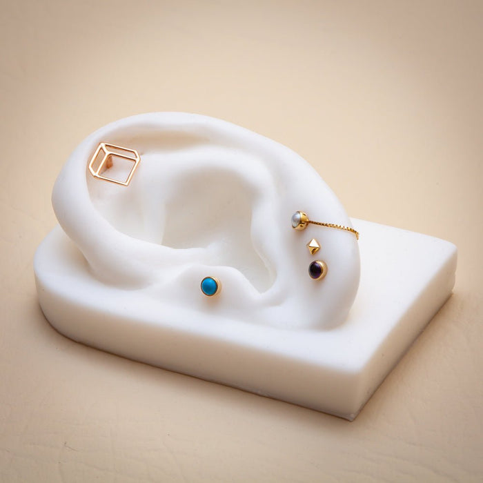 Gold flat back cabochon studs styled on white ear display alongside other gemstone piercing jewelry
