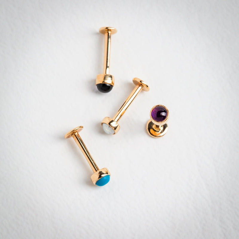Four 14k gold flat back labret studs laid flat showing opal, turquoise, amethyst, and black gemstone color options