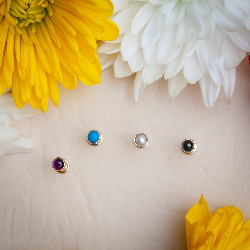 Top-down view of four 2mm bezel-set cabochon tops in pearl, turquoise, amethyst, and onyx on floral background