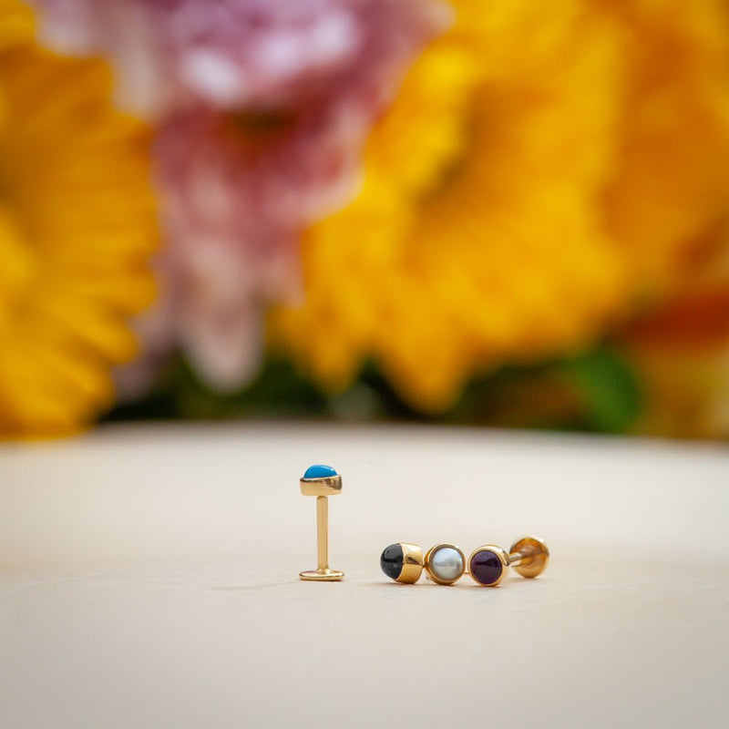 2mm turquoise cabochon flat back stud standing upright beside other stone options, floral background