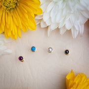 Top-down view of four 14k gold bezel cabochon stud ends: turquoise, pearl, black, and amethyst