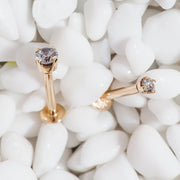 Two 14k rose gold 2mm diamond flat back labret studs resting on white decorative pebbles