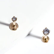 Two 14k yellow gold 2mm diamond flat back labret studs on white surface, top-down close-up view