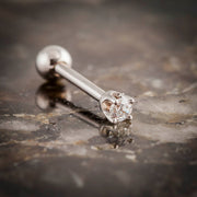 14k white gold 2mm CZ cartilage earring resting on stone surface, side profile showing post length