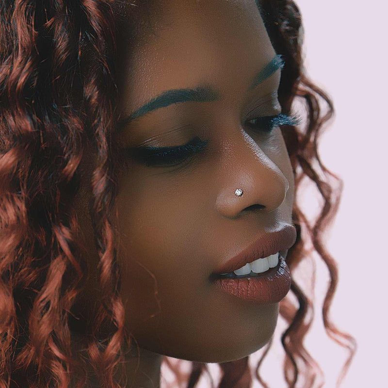 Small CZ prong flat back stud worn in nose piercing on a model with curly red hair