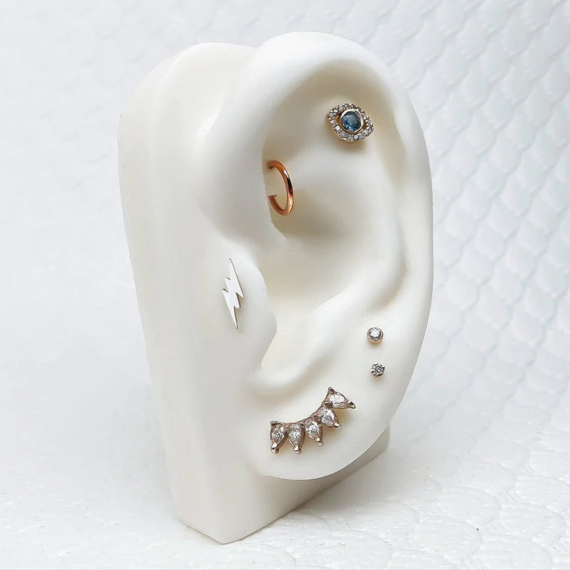 14k gold CZ flat back stud shown on white ear display with mixed piercing jewelry styling