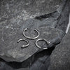 Three 950 platinum nose hoops in different diameters displayed on natural slate rock surface