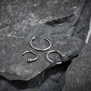 Three 950 platinum nose hoops in different diameters displayed on natural slate rock surface