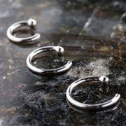 Three solid 950 platinum nose hoop rings in varying sizes arranged on dark stone surface