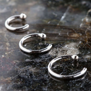 Three solid 950 platinum nose hoop rings in varying sizes arranged on dark stone surface