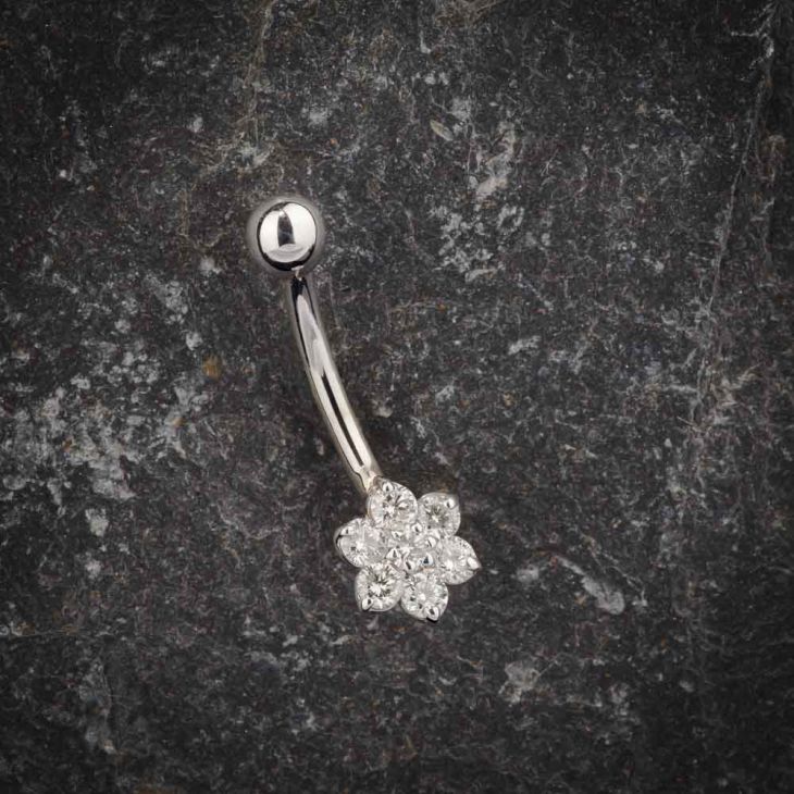 14k white gold diamond flower navel ring displayed on dark stone surface, angled view
