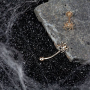 14K rose gold spider curved barbell and matching stud displayed on dark stone with cobweb styling