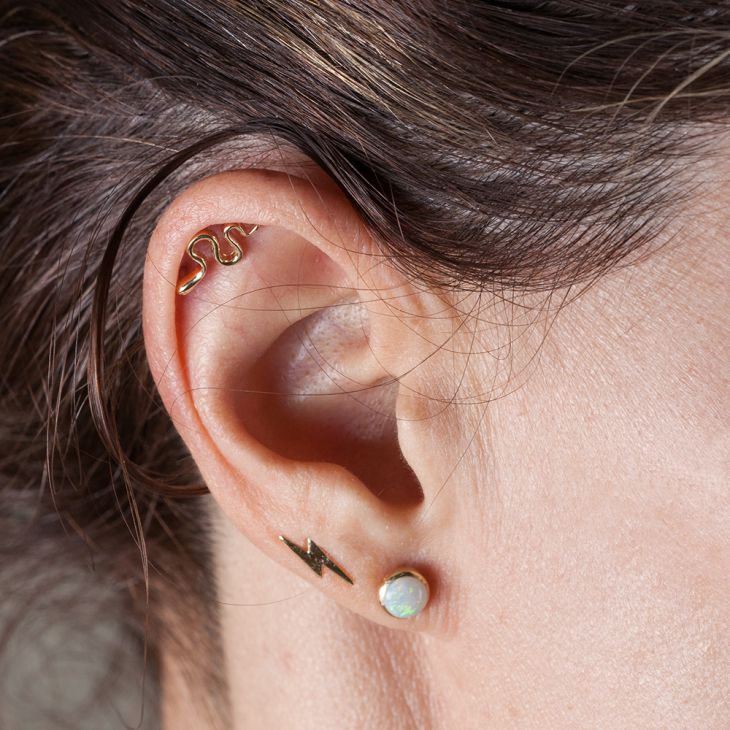Gold snake cartilage stud shown in helix piercing, styled with lightning bolt and opal lobe studs