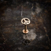 14K rose gold peace sign labret stud standing upright on dark stone surface, full profile view