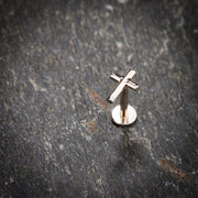 14K rose gold cross labret stud standing upright on slate stone surface for scale