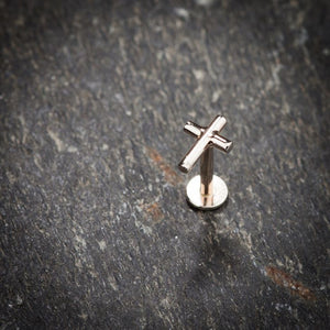 14K rose gold cross labret stud standing upright on slate stone surface for scale