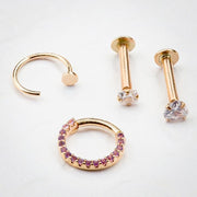 14K rose gold nail nose hoop styled with matching gold piercing jewelry on white surface