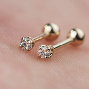 Two 14k gold diamond prong-set cartilage studs held against skin showing tiny size and sparkle