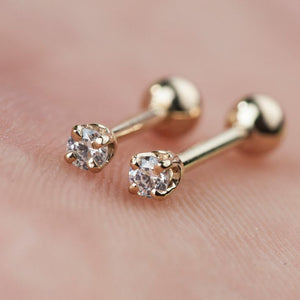 Two 14k gold diamond prong-set cartilage studs held against skin showing tiny size and sparkle