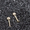 Two 14K yellow gold ball flat back labret studs in different lengths resting on dark textured surface