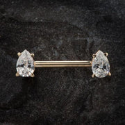 14K yellow gold straight barbell with clear pear-cut CZ ends, laid flat on dark stone surface