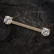 14k yellow gold industrial barbell with clear CZ ends resting on dark stone surface, angled lifestyle view