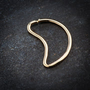 14K yellow gold moon-shaped seamless daith ring on dark stone surface, angled lifestyle view