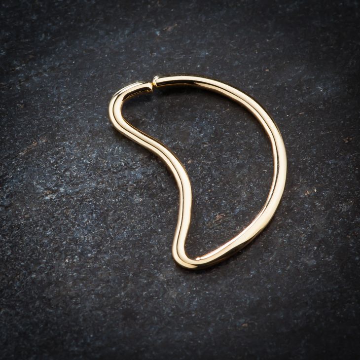 14K yellow gold moon-shaped seamless daith ring on dark stone surface, angled lifestyle view