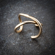 Angled side view of 14k yellow gold X band ear cuff resting on dark stone surface