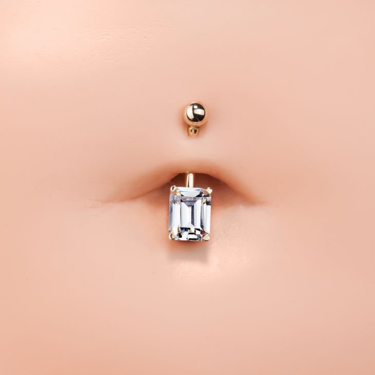 14k rose gold emerald-cut CZ navel ring shown in pierced belly button for fit and scale