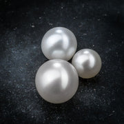 Three cultured pearl replacement balls in small, medium, and large sizes on dark surface for comparison