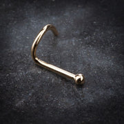 14K yellow gold tiny ball nose ring twist resting on dark stone surface, angled lifestyle view