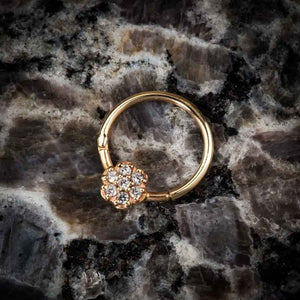 14K yellow gold diamond pavé flower clicker ring laid on dark marble stone surface