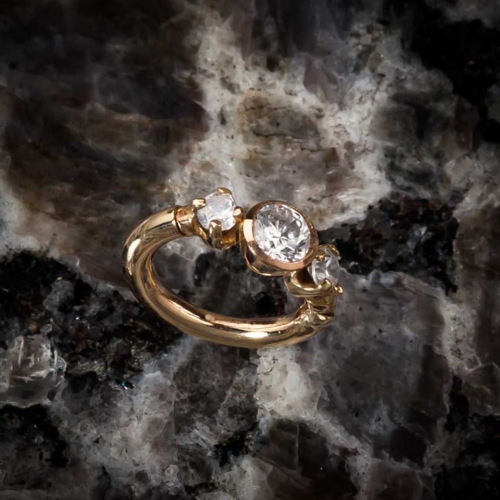 14k yellow gold three-CZ engagement-style clicker ring resting on dark marble surface