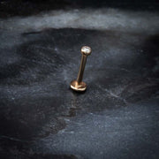 14k rose gold bezel-set diamond flat back labret standing upright on dark stone surface, lifestyle shot