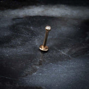14k rose gold 2mm CZ bezel flat back labret standing upright on dark stone surface