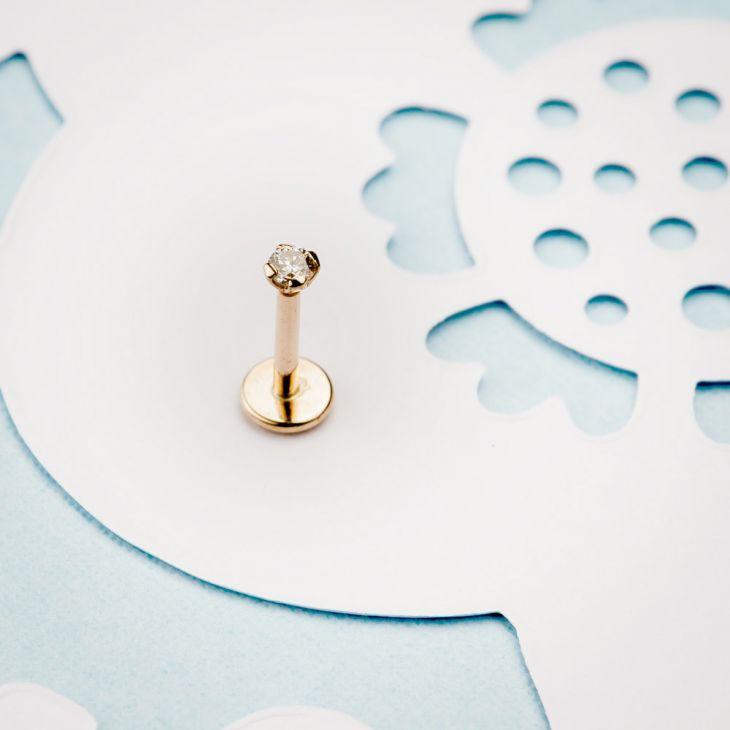 14k rose gold diamond labret flat back stud standing upright on decorative blue and white paper background