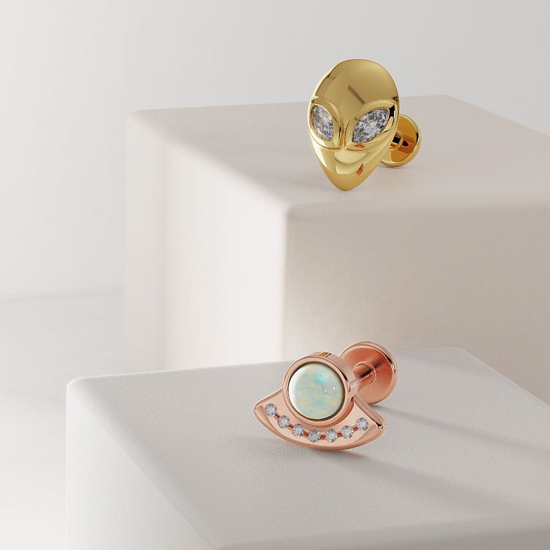 14K yellow gold alien diamond labret displayed alongside a rose gold UFO opal flat back earring