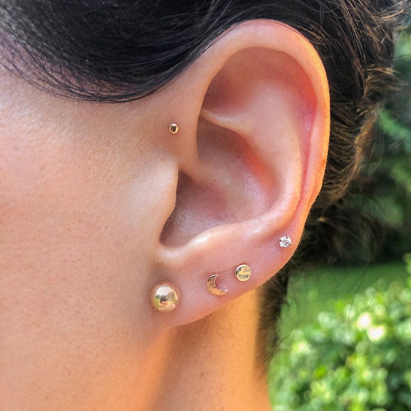 Curated ear stack featuring gold flat back diamond stud in helix and lobe piercings on a model