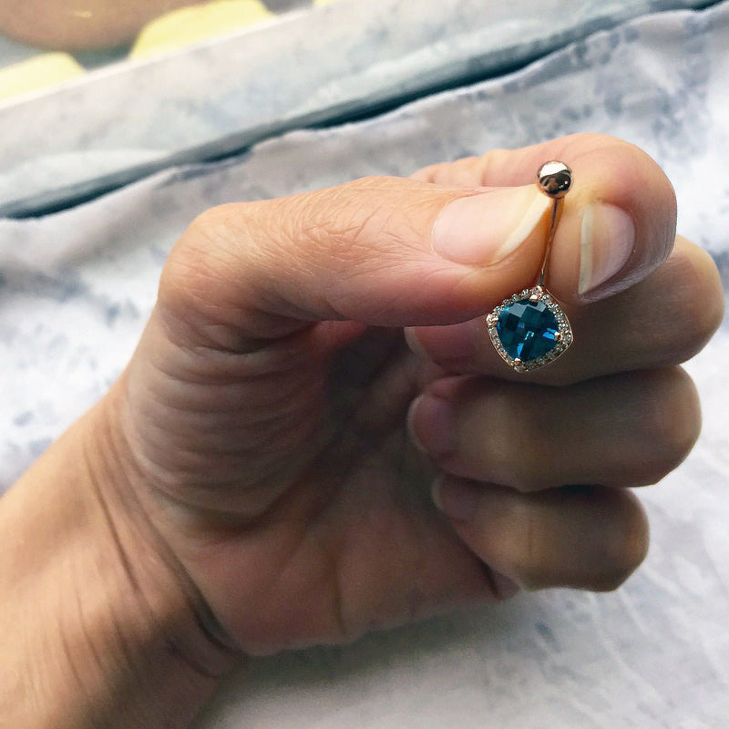 Swiss blue topaz diamond 14k gold navel ring held between fingers for size reference