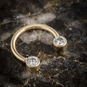 Angled top-down view of 14k yellow gold CZ circular barbell laid flat on dark crystal surface