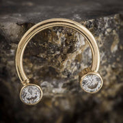 14k yellow gold CZ circular barbell resting against rough stone surface, lifestyle detail shot